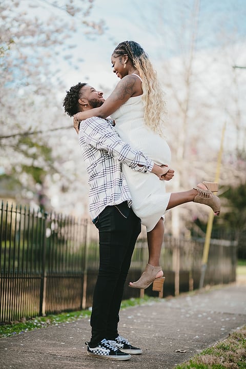 Man lifts his fiancée under spring cherry blossoms