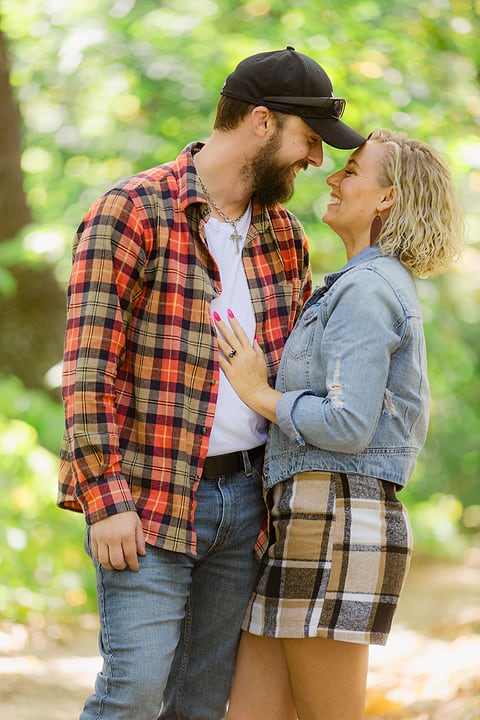 Couple in flannel and denim touching foreheads in the woods