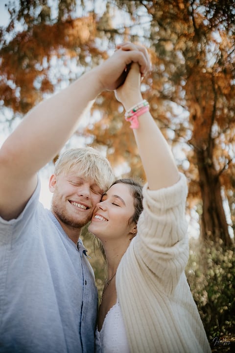 Couple dancing with raised hands under fall trees