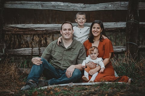 Family with a baby sitting by a rustic wooden fence