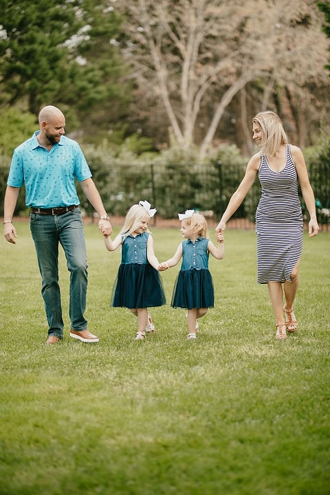 Parents and two daughters walking hand in hand on a lawn
