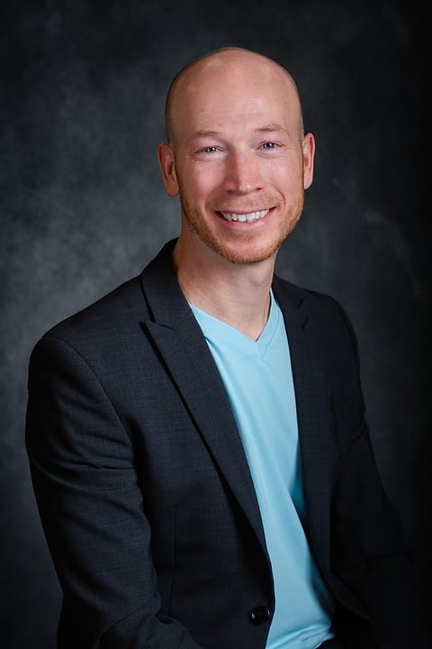 Studio headshot of a smiling man in a navy blazer