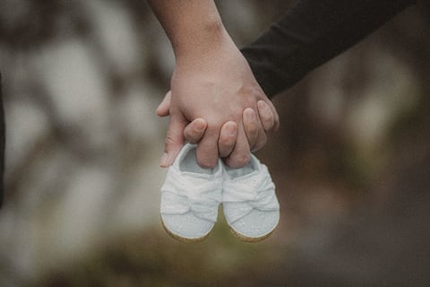 Hands holding tiny white baby shoes