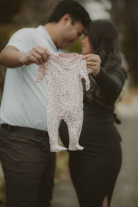 Parents-to-be holding up a tiny baby outfit