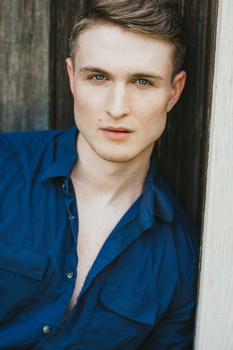 Male model in a blue shirt by a wooden door