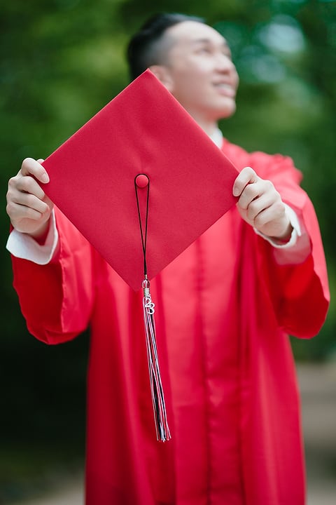 Graduate holding up a red cap and tassel