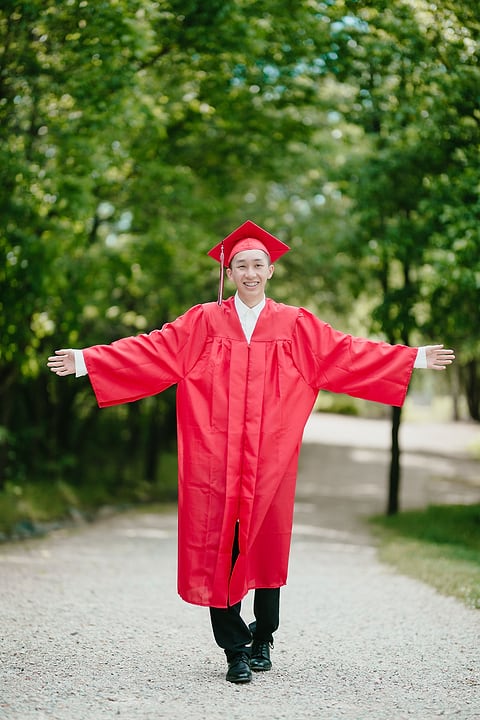 Graduate with arms outstretched on a tree-lined path