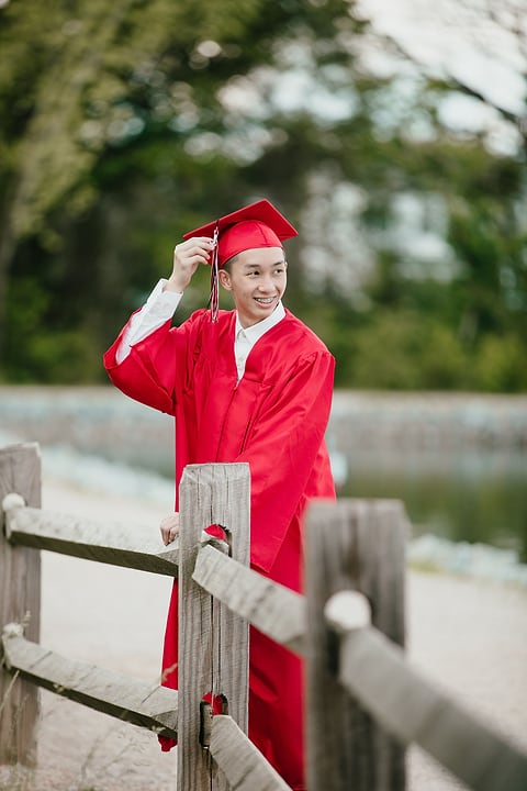 Graduate adjusting his cap by a lake fence