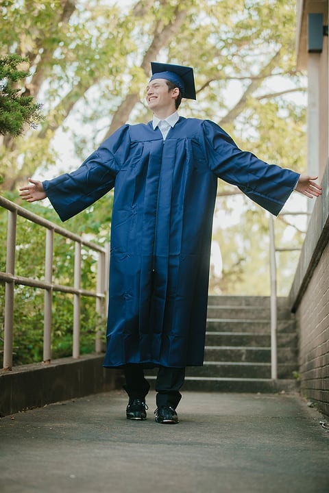 Graduate celebrating with arms wide on campus steps