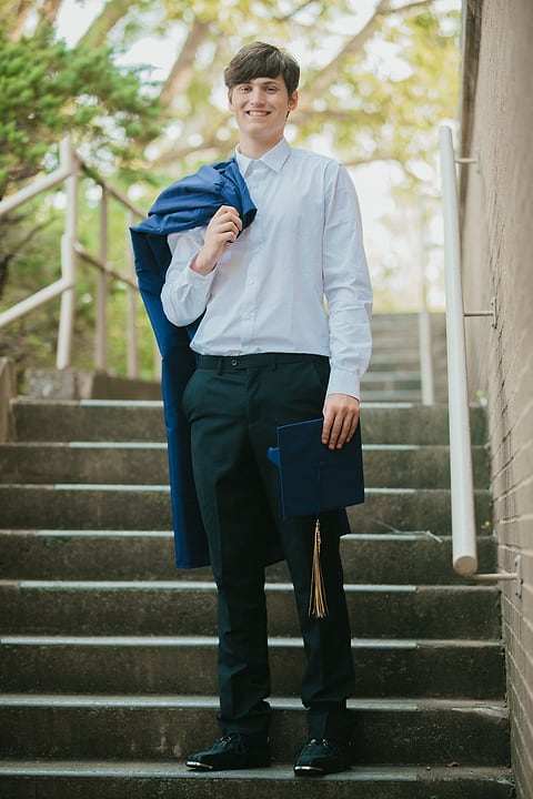 Senior portrait on outdoor stairs with gown over shoulder
