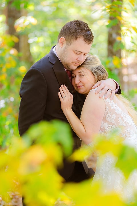 Bride and groom embrace among autumn leaves